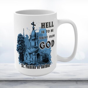 May include: White ceramic mug with a blue and gray illustration of a church with the text "Hell is to be away from God" and "St. Paisios of Athos".