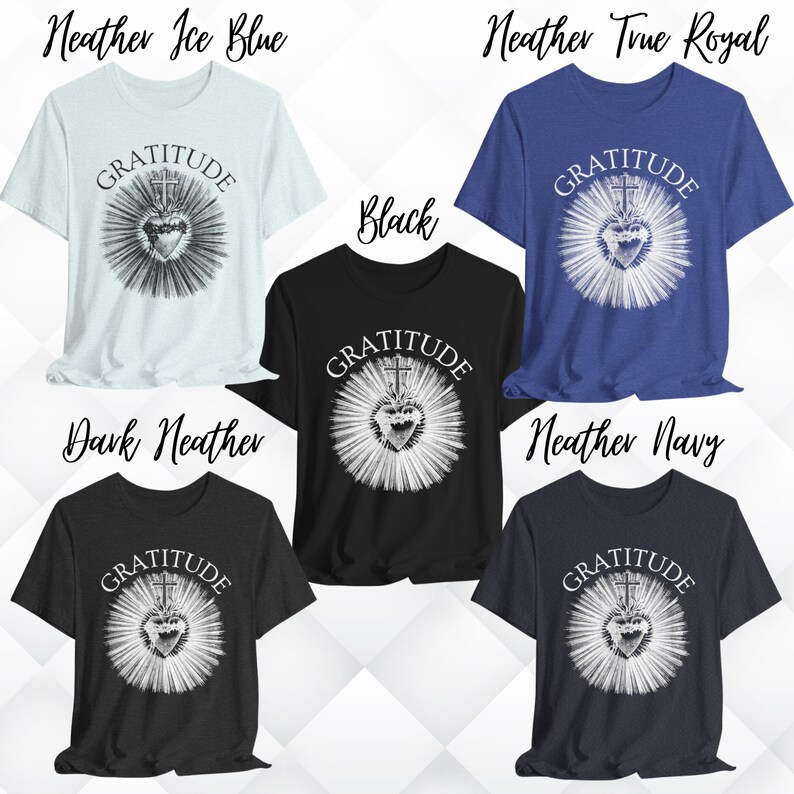Może przedstawiać: Pięć koszulek z kr&oacute;tkim rękawem w kolorach heather ice blue, heather true royal, czarnym, dark heather i heather navy. Każda koszulka posiada białą grafikę serca z krzyżem i promieniami oraz nadrukowane łukiem słowo GRATITUDE powyżej.