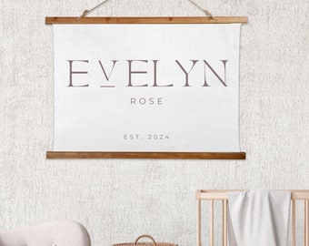 May include: A white canvas wall hanging with the name "Evelyn Rose" and the text "Est. 2024" in a brown font. The hanging is attached to a wooden dowel rod.
