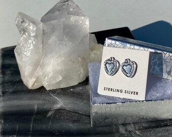 May include: A pair of sterling silver heart-shaped earrings in a small white box with a silver background. The earrings are on a white card with the text "Sterling Silver".
