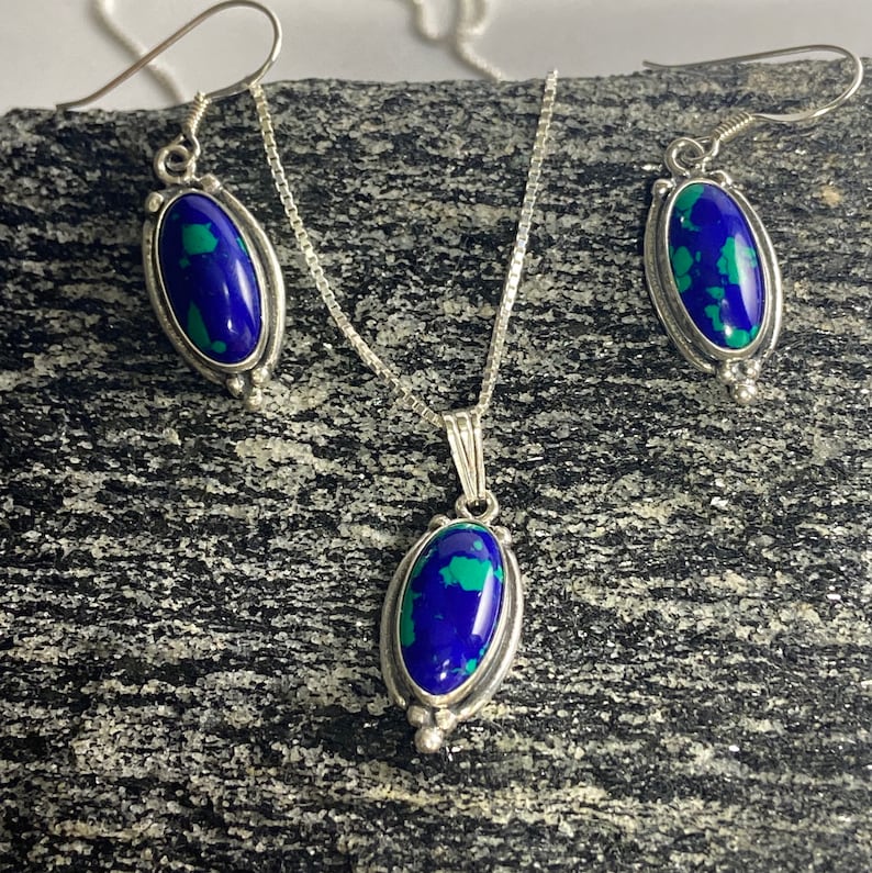 May include: A silver necklace and earrings set with oval-shaped blue and green gemstone pendants.