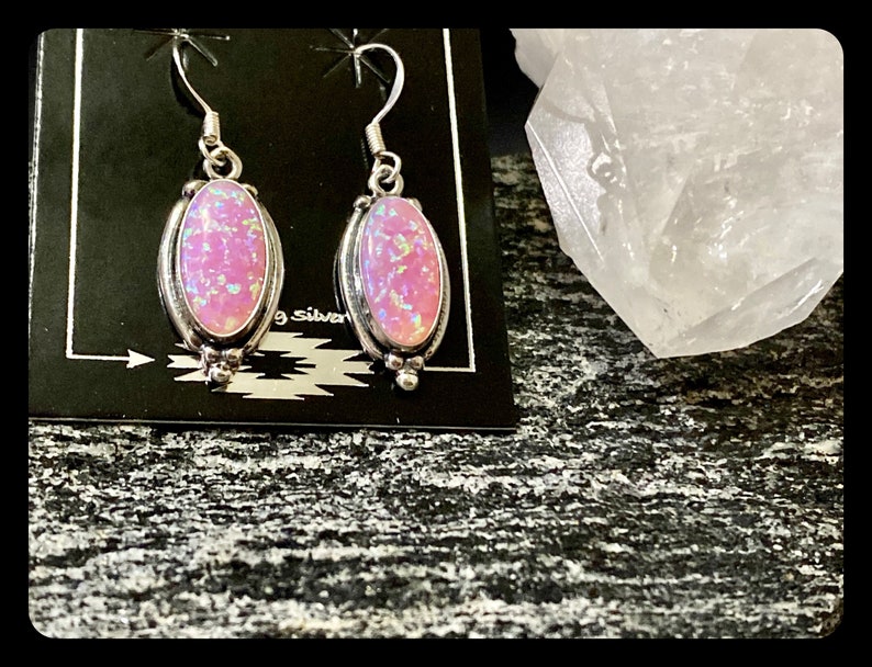 K&ouml;nnte beinhalten: Ein Paar silberne Ohrh&auml;nger mit rosafarbenen Opal-Steinen. Die Ohrringe haben ein schlichtes Design mit einem kleinen ovalen Stein.