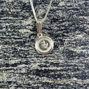 May include: A silver necklace with a round pendant featuring a delicate etched leaf design.