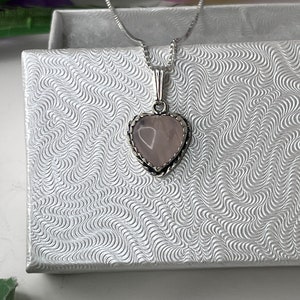 Puede incluir: Un collar de cadena de plata con un colgante en forma de coraz&oacute;n con una piedra de cuarzo rosa. El colgante tiene un delicado borde de plata.