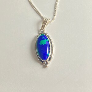 May include: A silver chain necklace with a pendant featuring a blue and green oval gemstone set in a silver bezel.