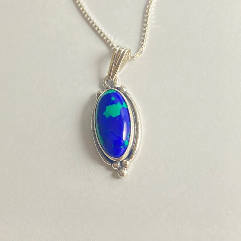 May include: A silver chain necklace with a pendant featuring a blue and green oval gemstone set in a silver bezel.