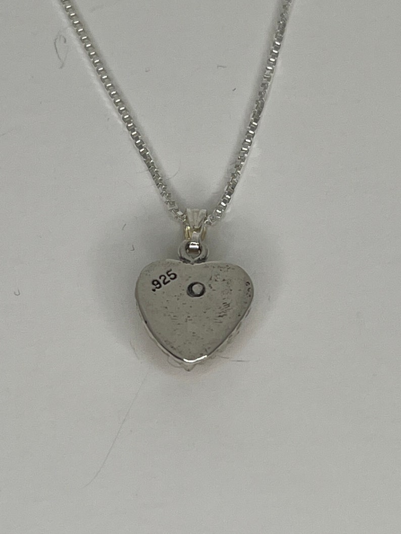 Puede incluir: Un collar de plata con un colgante en forma de coraz&oacute;n y una cadena. La parte posterior del colgante est&aacute; estampada con el n&uacute;mero "925".