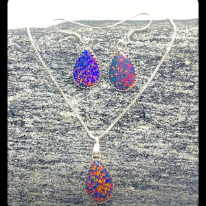 May include: A silver necklace and earrings set with teardrop-shaped opal pendants. The opals are iridescent with shades of blue, red, and green.