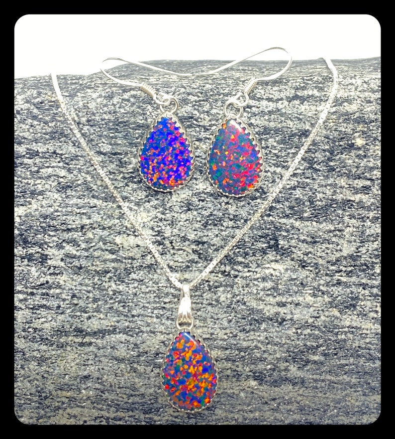 May include: A silver necklace and earrings set with teardrop-shaped opal pendants. The opals are iridescent with shades of blue, red, and green.