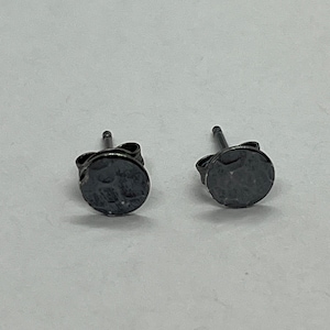 May include: A pair of small, round, black stud earrings with a hammered texture.
