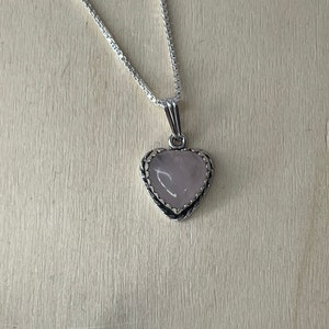 Puede incluir: Un collar de cadena de plata con un colgante en forma de coraz&oacute;n con una piedra preciosa rosa p&aacute;lida.