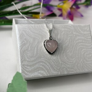 Puede incluir: Un collar de cadena de plata con un colgante de coraz&oacute;n rosa. El colgante tiene un borde plateado y un dise&ntilde;o delicado.