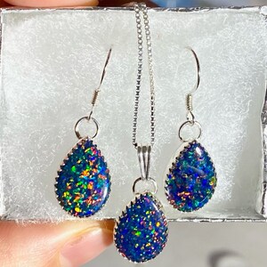 May include: A silver necklace and earrings set with teardrop-shaped opal pendants. The opals are iridescent with blue, green, and orange hues.