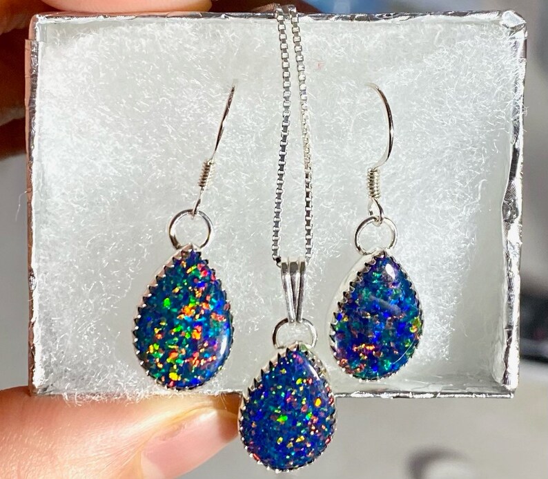 May include: A silver necklace and earrings set with teardrop-shaped opal pendants. The opals are iridescent with blue, green, and orange hues.