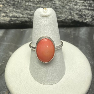 May include: A silver ring with a large oval-shaped pink gemstone.