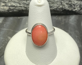 May include: A silver ring with a large oval-shaped pink gemstone.