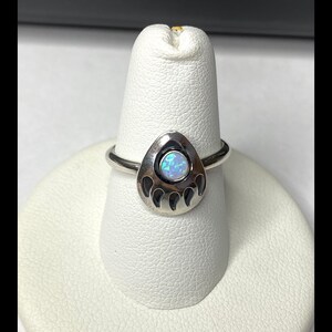 May include: A silver ring with a bear paw print design featuring an iridescent opal stone.