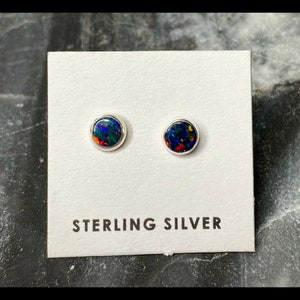 May include: A pair of sterling silver stud earrings with round black opal stones. The earrings are displayed on a white card with the text "Sterling Silver".