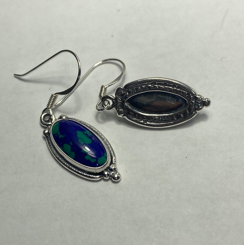 May include: A pair of silver earrings with oval-shaped blue and green gemstone settings. The earrings have a delicate, ornate design.