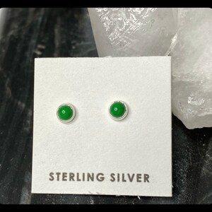 May include: A pair of sterling silver stud earrings with green gemstone accents. The earrings are displayed on a white card with the text "STERLING SILVER".