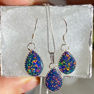 May include: A silver necklace and earrings set with teardrop-shaped black opal stones. The opals have a rainbow iridescent sheen.