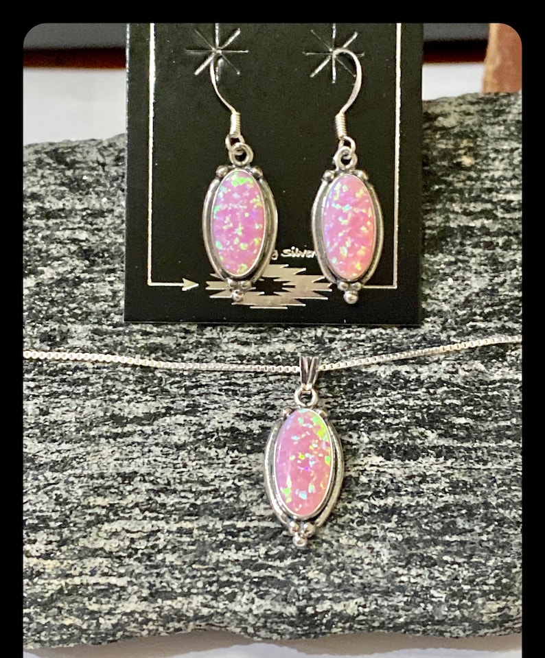 K&ouml;nnte beinhalten: Ein Set aus pinken Opal-Ohrringen und einer Halskette mit Anh&auml;nger. Die Ohrringe und der Anh&auml;nger sind oval geformt und in Silber gefasst.
