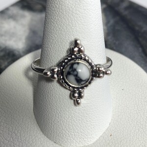 May include: A silver ring with a white and black marbled stone set in a decorative design.
