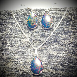 May include: A silver necklace and earrings set with teardrop-shaped opal stones. The opals have a dark base with iridescent flashes of blue, green, and red.