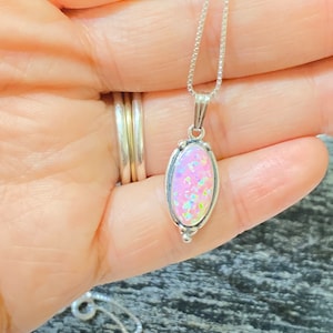K&ouml;nnte beinhalten: Eine silberne Kettenkette mit einem rosa Opal-Anh&auml;nger. Der Anh&auml;nger ist oval geformt und in einer silbernen Fassung gefasst.