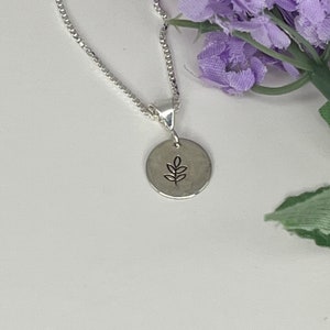 May include: A silver chain necklace with a small, round pendant featuring a simple leaf design.