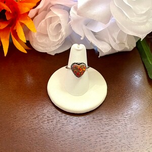 May include: A silver ring with a heart-shaped opal gemstone. The opal is a mix of red, orange, and yellow.