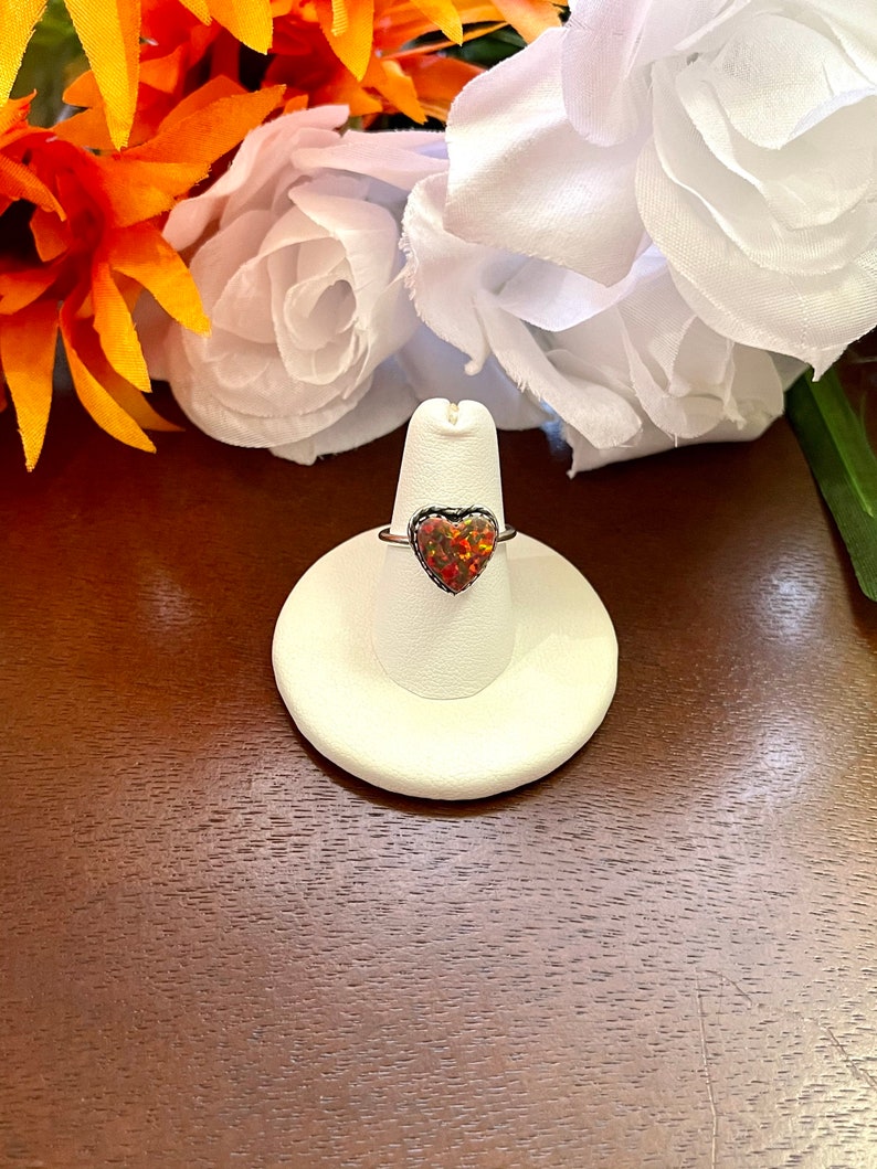 May include: A silver ring with a heart-shaped opal gemstone. The opal is a mix of red, orange, and yellow.