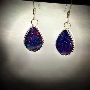 May include: A pair of silver teardrop earrings with a dark blue, red, and green iridescent opal stone set in each earring.