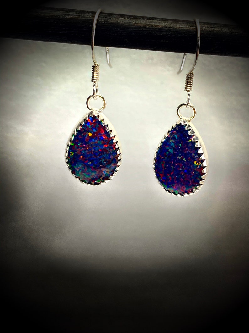 May include: A pair of silver teardrop earrings with a dark blue, red, and green iridescent opal stone set in each earring.