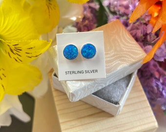 Könnte beinhalten: Ein Paar blaue Opal-Ohrstecker in einer kleinen weißen Schachtel mit der Aufschrift "STERLING SILVER" auf der Vorderseite.