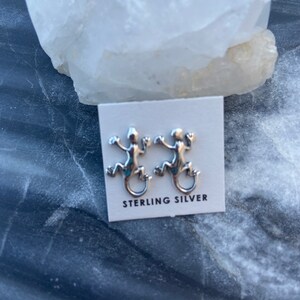 May include: A pair of sterling silver lizard earrings. The lizards are facing to the right and have detailed features.