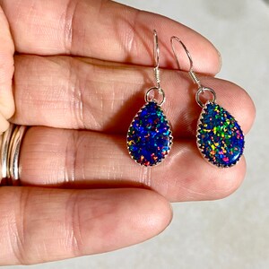 May include: A pair of silver teardrop earrings with iridescent blue, green, and red opal stones.