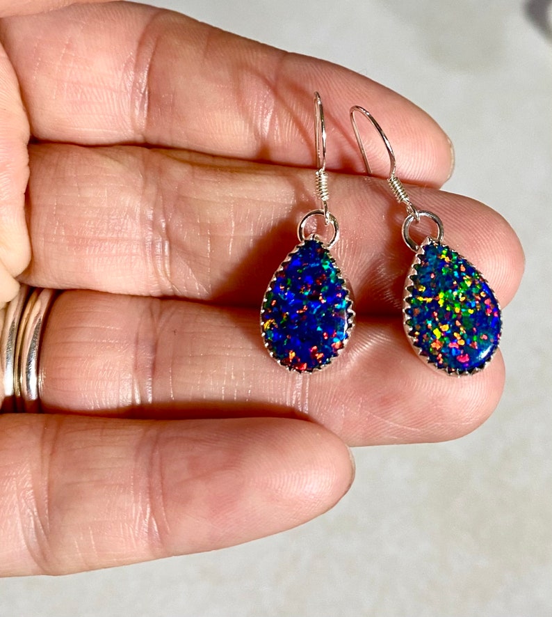 May include: A pair of silver teardrop earrings with iridescent blue, green, and red opal stones.