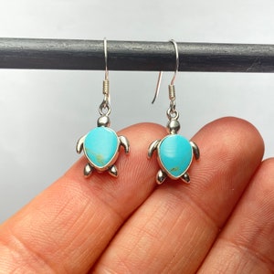 May include: Sterling silver earrings featuring a turquoise turtle design. The earrings are dangle style with a hook closure.