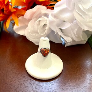 May include: A silver ring with a heart-shaped opal gemstone. The opal is a mix of orange, red, and yellow.