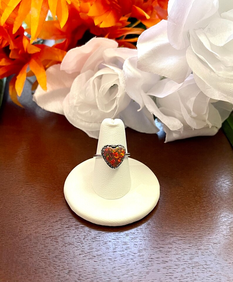 May include: A silver ring with a heart-shaped opal gemstone. The opal is a mix of orange, red, and yellow.