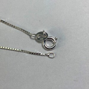 May include: A silver chain necklace with a lobster clasp and a small jump ring. The chain is box style and has a polished finish.