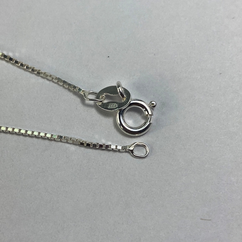 May include: A silver chain necklace with a lobster clasp and a small jump ring. The chain is box style and has a polished finish.