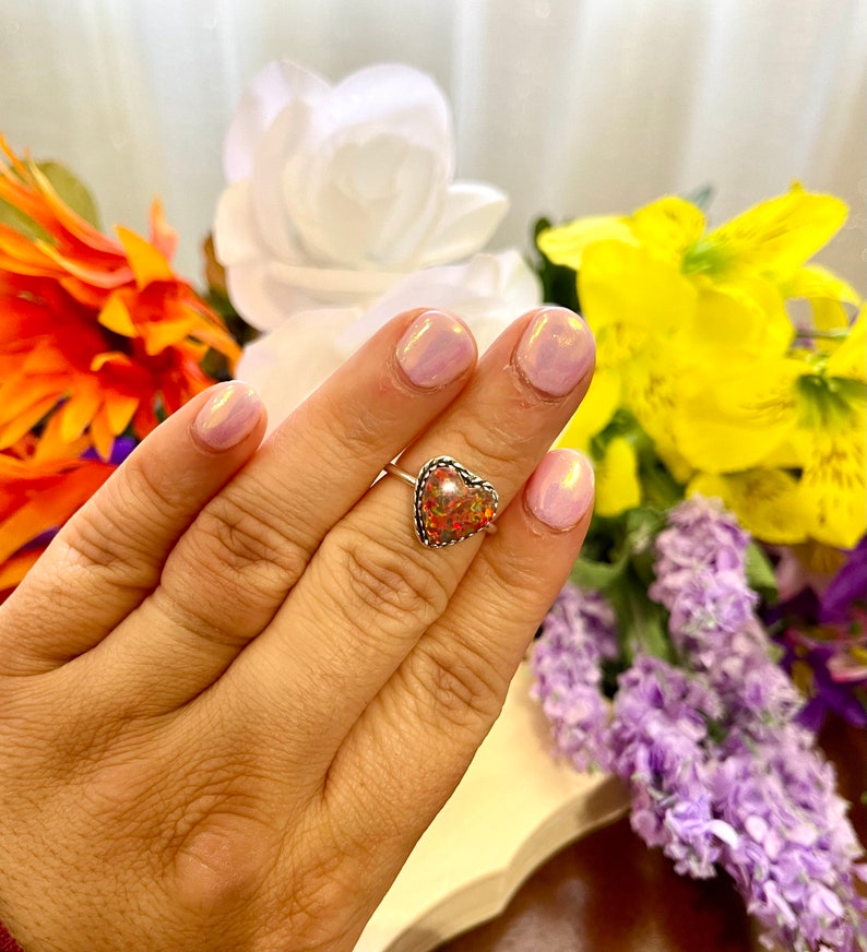 May include: A silver ring with a heart-shaped opal stone. The opal is a mix of pink, orange, and yellow.