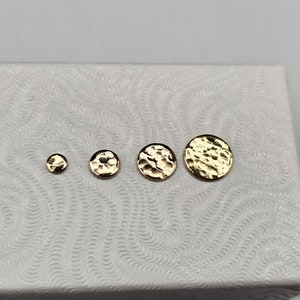 May include: Four gold-colored hammered metal discs of varying sizes, displayed on a white surface.