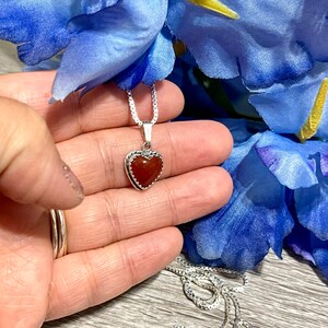 K&ouml;nnte beinhalten: Eine silberne Kettenkette mit einem herzf&ouml;rmigen Anh&auml;nger mit einem roten Karneol-Stein.