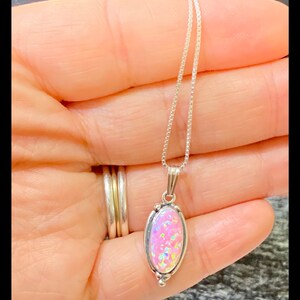 K&ouml;nnte beinhalten: Eine silberne Kettenkette mit einem ovalen Anh&auml;nger aus rosa Opal. Der Anh&auml;nger ist mit Silber gefasst und von einem silbernen Rand umgeben.