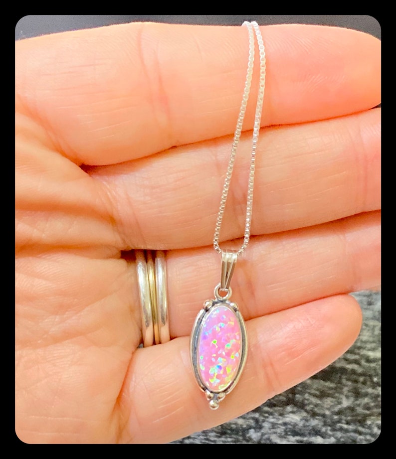 K&ouml;nnte beinhalten: Eine silberne Kettenkette mit einem ovalen Anh&auml;nger aus rosa Opal. Der Anh&auml;nger ist mit Silber gefasst und von einem silbernen Rand umgeben.