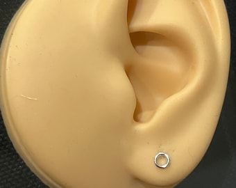 Può includere: Un primo piano di un orecchino a cerchio d'argento su un orecchio di manichino. L'orecchino è un semplice cerchio sottile.