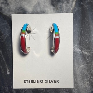 May include: A pair of sterling silver hoop earrings with red, white, turquoise, and green inlay. The earrings are on a white card with the text "STERLING SILVER".